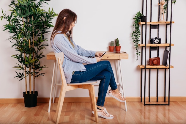 Ragazza con smartphone seduto al posto di lavoro