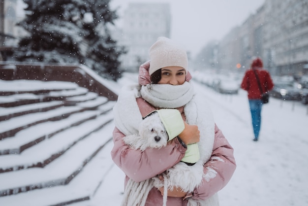 Ragazza con un cane in braccio su una strada cittadina la neve sta cadendo