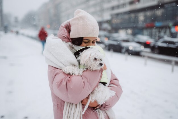 Ragazza con un cane in braccio su una strada cittadina la neve sta cadendo