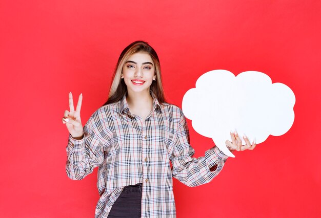 Ragazza con un maglione caldo che tiene in mano un'ideaboard a forma di nuvola e nomina la persona davanti