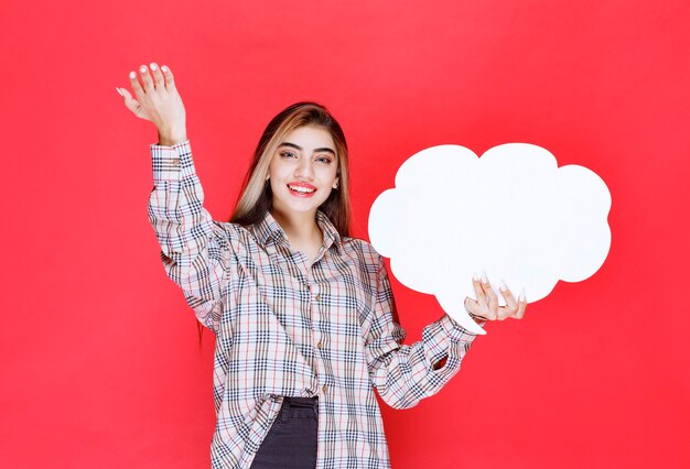 Ragazza con un maglione caldo che tiene in mano un'ideaboard a forma di nuvola e nomina la persona davanti