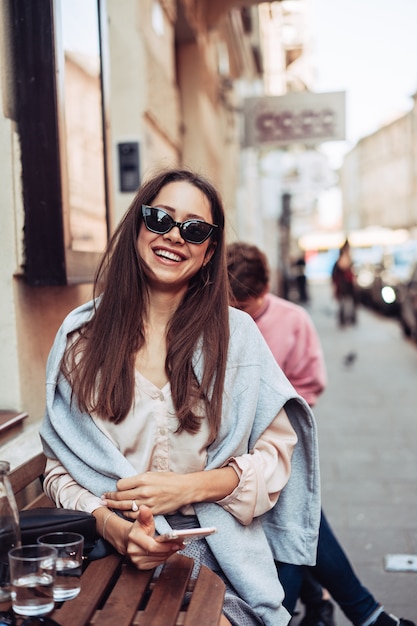 Ragazza con uno smartphone che si siede in un caffè della via.