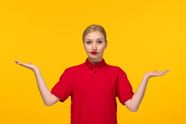 Ragazza confusa di giorno della camicia rossa agitando le mani in aria in una camicia rossa su sfondo giallo