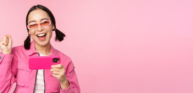 Ragazza coreana sorridente felice che vince sul telefono cellulare guardando lo schermo orizzontale dello smartphone e si rallegra