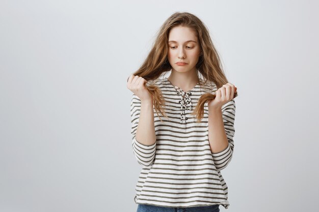 Ragazza cupa che guarda i suoi capelli, ha bisogno di un nuovo taglio di capelli