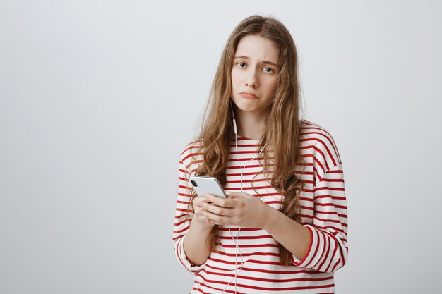 Ragazza cupa sconvolta che sembra angosciata durante l'utilizzo di telefoni cellulari e auricolari