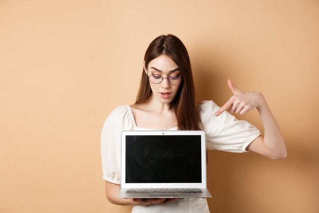 Ragazza curiosa con gli occhiali che punta allo schermo del laptop controlla l'accordo online dimostra il progetto su compu...