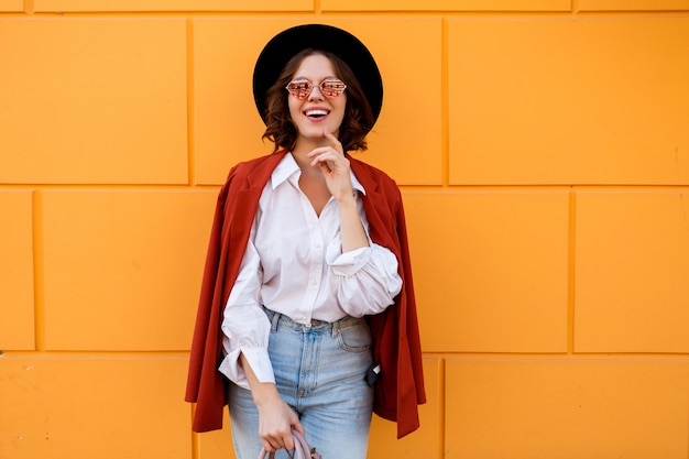 Ragazza dai capelli corti sorridente felice che posa sopra la parete gialla. Colori caldi. umore positivo.