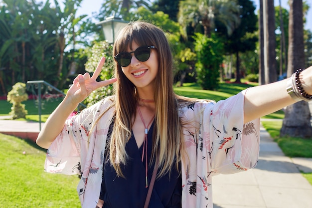 Ragazza dai capelli lunghi sorridente in viaggio gioiosa che fa autoritratto sulla strada a Los Angeles.