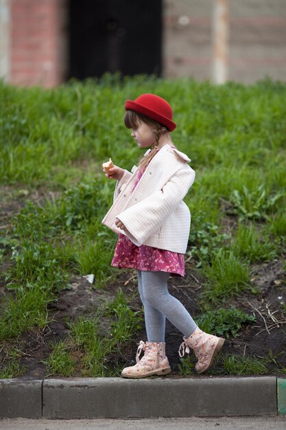 Ragazza del bambino con le trecce in cappello che mangia il gelato e cammina