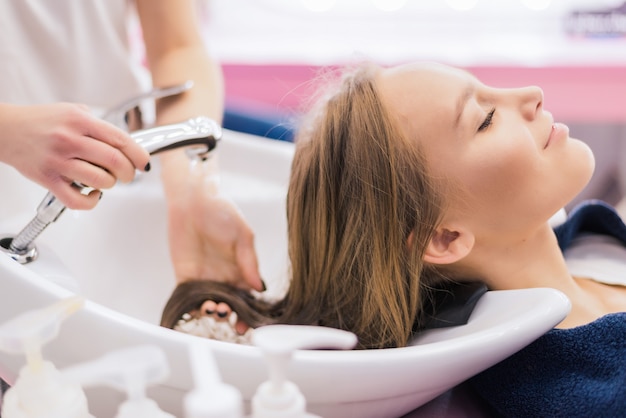 Ragazza del barbiere che pettina i suoi capelli nel salone di bellezza. Bella signora che ha i capelli lavati dal parrucchiere nel salone di parrucchiere.