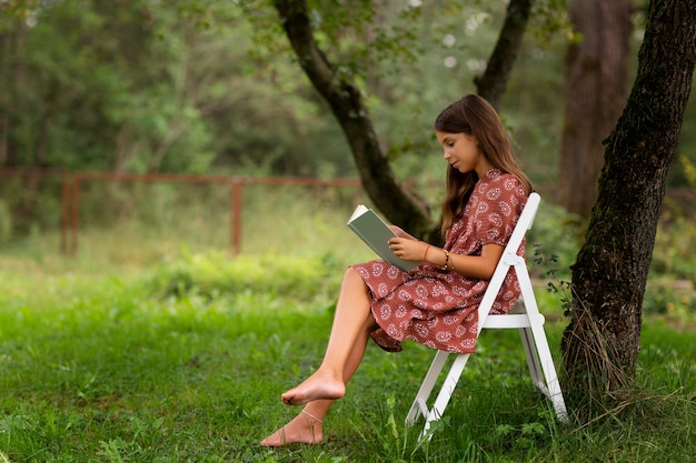 Ragazza del colpo pieno che legge in natura