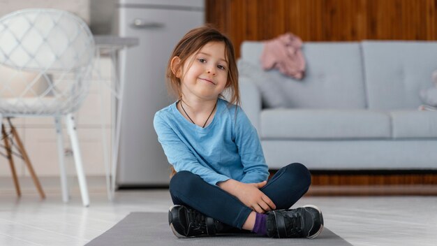 Ragazza del colpo pieno che si siede sulla stuoia di yoga