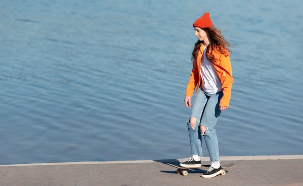 Ragazza del colpo pieno su skate in riva al lago