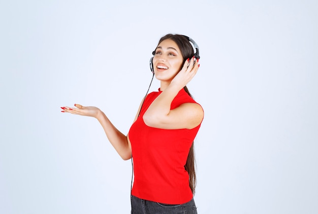 Ragazza del DJ in camicia rossa con le cuffie che indica qualcosa o che mostra qualcosa in mano.