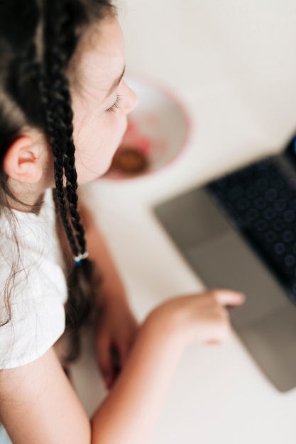 Ragazza del primo piano con le trecce che esaminano computer portatile