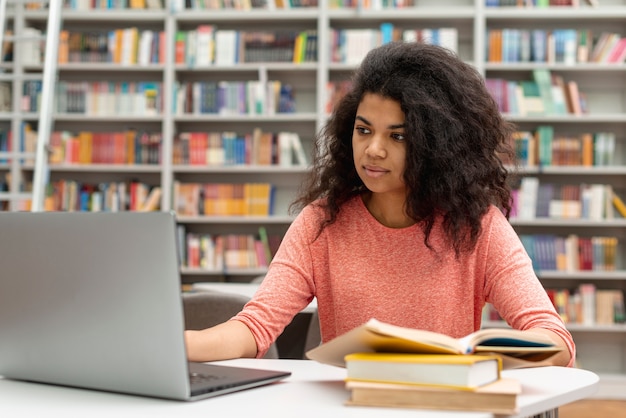 Ragazza dell'angolo alto alla biblioteca che studia e che per mezzo del computer portatile