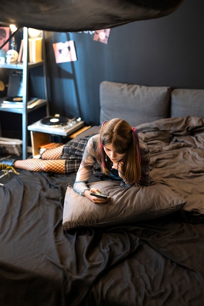 Ragazza dell'angolo alto con lo smartphone a letto