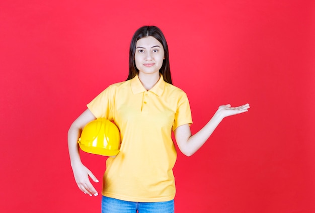 Ragazza dell'ingegnere in dresscode giallo che tiene un casco di sicurezza giallo.