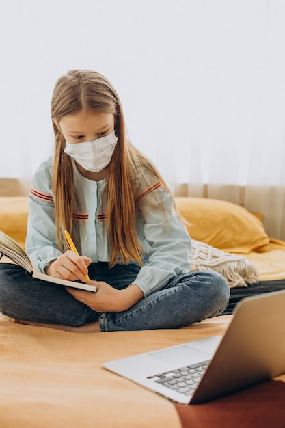 Ragazza della scuola che studia a casa che indossa la maschera, apprendimento a distanza