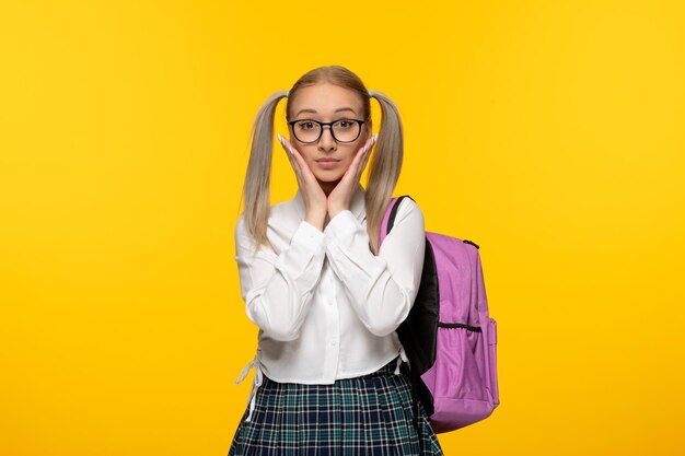 Ragazza della scuola eccitata giornata mondiale del libro in uniforme con zaino rosa su sfondo giallo