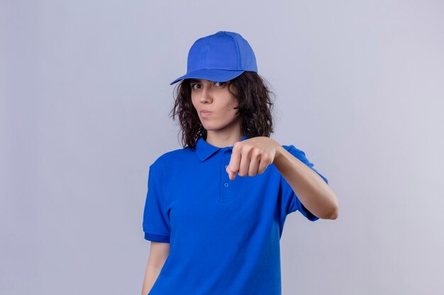 Ragazza delle consegne in uniforme blu e cappuccio che gesturing l'urto del pugno come se salutasse guardando con espressione sospettosa in piedi sopra lo spazio bianco isolato