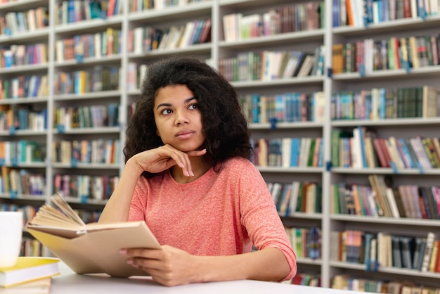 Ragazza di angolo basso alla lettura delle biblioteche