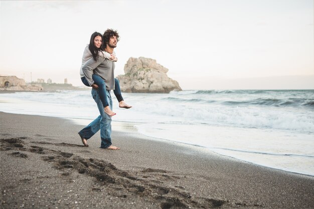 Ragazza di arrampicata sulla schiena di un uomo sulla spiaggia