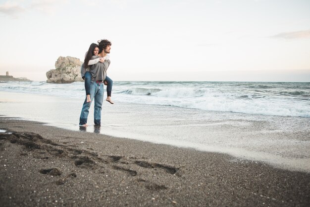 Ragazza di arrampicata sulla schiena di un uomo sulla spiaggia