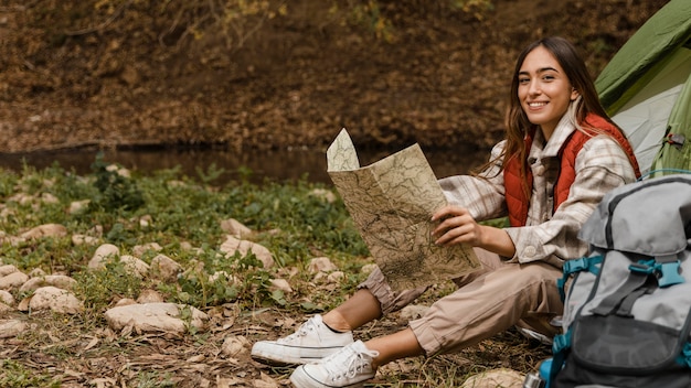 Ragazza di campeggio felice nella foresta che controlla il colpo lungo della mappa