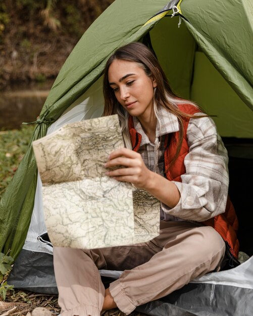 Ragazza di campeggio felice nella foresta che controlla la mappa