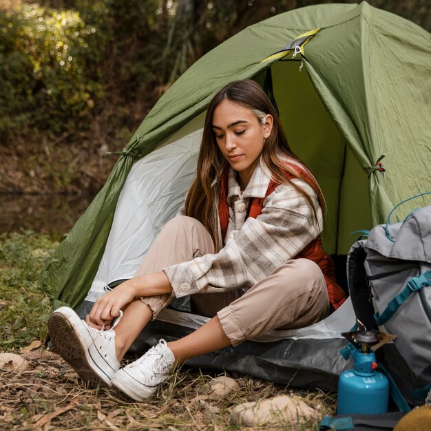 Ragazza di campeggio felice nella foresta che lega i suoi lacci