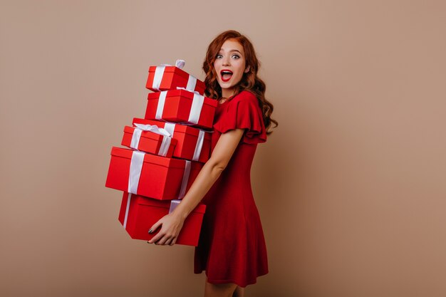 Ragazza di compleanno allegra in vestito che propone con i regali. Felice giovane modello femminile in possesso di regali di Capodanno.