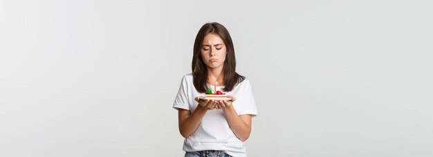 Ragazza di compleanno miserabile che sembra triste per la torta di compleanno con la candela