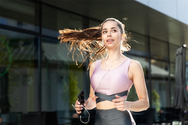 Ragazza di forma fisica che ascolta la musica che corre di mattina