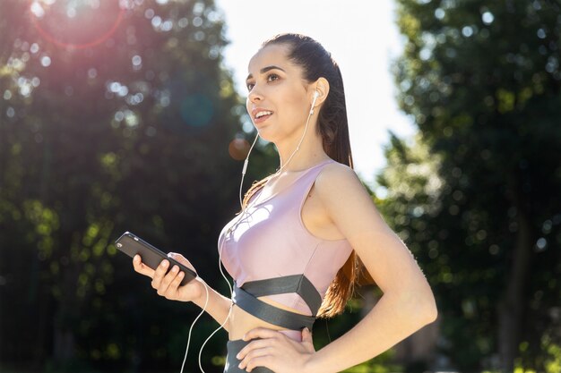 Ragazza di forma fisica nell'abbigliamento sportivo alla moda che ascolta la musica si trova sulla strada