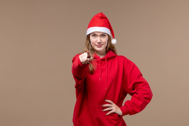 Ragazza di natale di vista frontale che sorride e che indica sul natale di festa della donna del fondo marrone