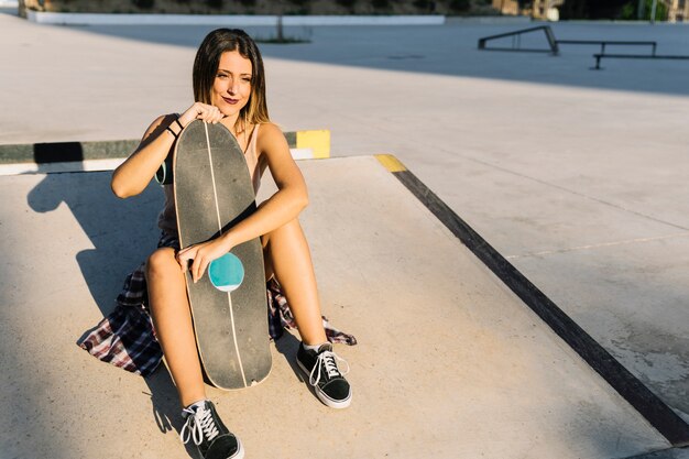 Ragazza di pattinatore che si siede con il bordo