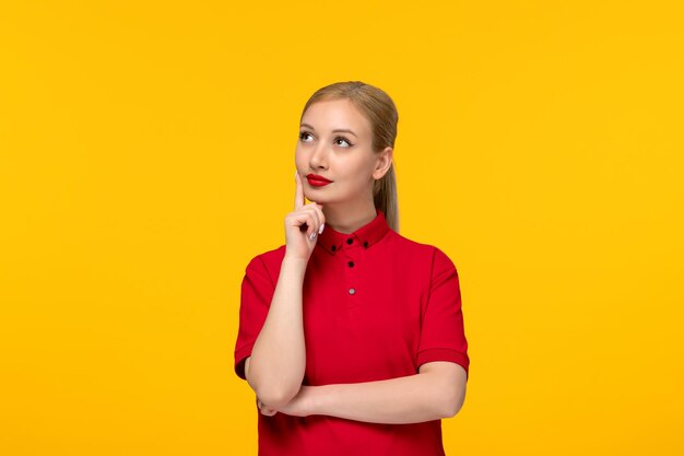 Ragazza di pensiero di giorno della camicia rossa che osserva in su in una camicia rossa su una priorità bassa gialla