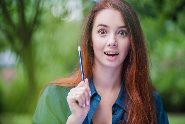 Ragazza di Redhead che esamina la matita della holding della macchina fotografica