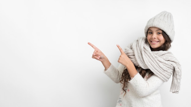 Ragazza di smiley con indicare della sciarpa e del cappello