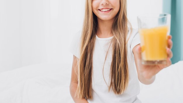 Ragazza di smiley di vista frontale che tiene un bicchiere di succo d'arancia