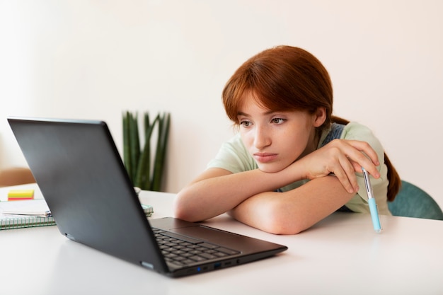 Ragazza di tiro medio che studia con il computer portatile a casa