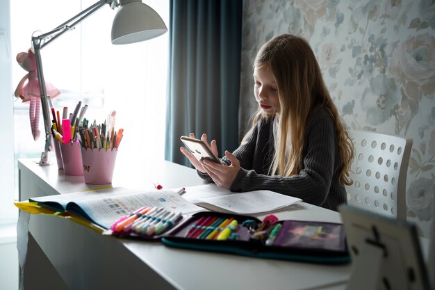 Ragazza di tiro medio con smartphone alla scrivania