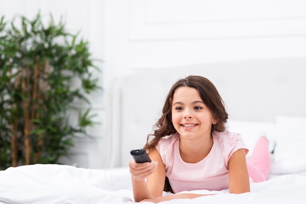 Ragazza di vista frontale a letto facendo uso del telecomando della TV