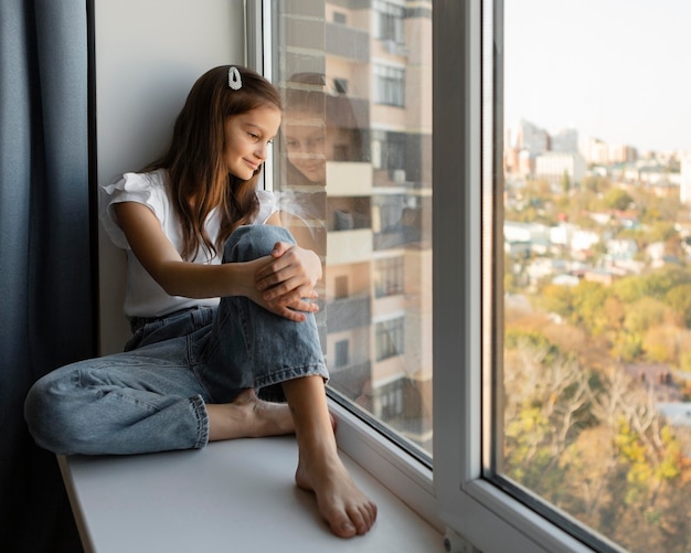 Ragazza di vista laterale che osserva fuori dalla finestra a casa