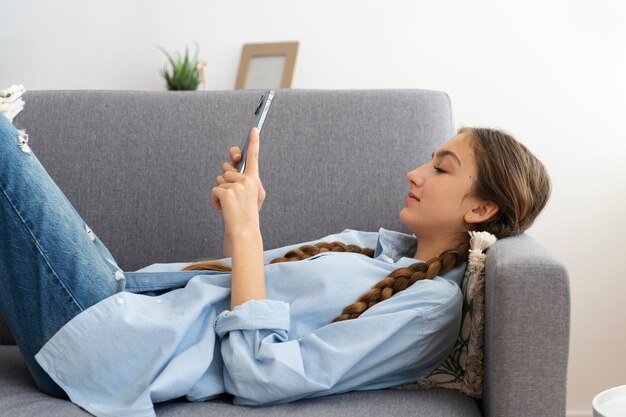 Ragazza di vista laterale sul divano con lo smartphone