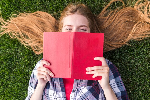 Ragazza di vista superiore che copre la bocca con un libro