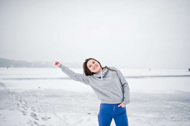 Ragazza divertente indossare su maglione con cappuccio e jeans al lago ghiacciato nella giornata invernale