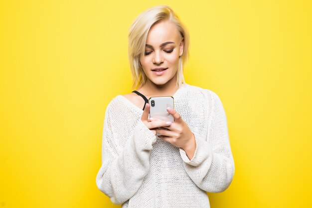 Ragazza donna giovane signora occupata in maglione bianco utilizza smartphone su giallo